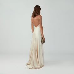 the back of a woman in a white dress with a gold clutch on her shoulder