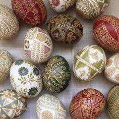 an assortment of painted easter eggs on a white tablecloth with gold and red designs