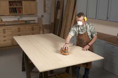 a man in an apron sanding down a table with a sander on it