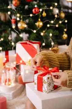 a woman opening a wrapped gift box in front of a christmas tree