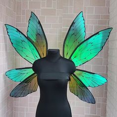 a black mannequin with green and yellow wings on it's body in front of a brick wall