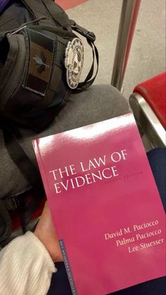 a pink book sitting on top of a person's lap next to a backpack