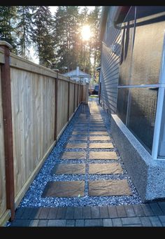 a wooden fence next to a building with gravel on the ground and trees in the background