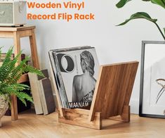 wooden vinyl record flip rack in front of a white wall with plants and pictures on it