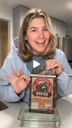 a woman sitting at a kitchen counter holding up a box of kodiak power cake mix