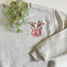 Our monogram reindeer sweatshirts are embroidered on our best selling crewneck sweatshirts. Choose your monogram font style. The design colors of the reindeer's antlers and lights will be as shown (light brown, light grey, red, kelly green, and royal blue) with a red monogram. PRODUCT DETAILS: Adult Unisex Sizes - 8 oz., pre-shrunk 50/50 cotton/polyester NuBlend® pill-resistant fleece High stitch density for a smooth printing canvas Seamless body with set-in sleeves 1x1 ribbed collar, cuffs and Christmas Shirt Embroidery Designs, Christmas Embroidery Sweatshirts, Monogram Clothes, Holiday Loungewear, Reindeer Lights, Charleston Wv, Circle Font, Monogram Sweatshirt, Monogram Shirts