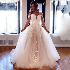 a woman in a white wedding dress standing on a wooden floor with her hands behind her back