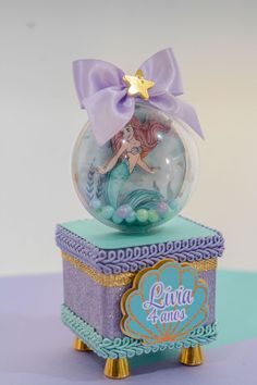 a glass ball with a little mermaid on it sitting on top of a purple box