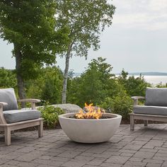 a fire pit sitting on top of a brick patio next to two chairs and a table