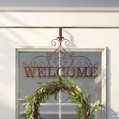 a welcome sign hanging from the side of a white building with a wreath on it