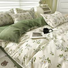 a bed with green and white comforters, pillows and a book on the pillowcase