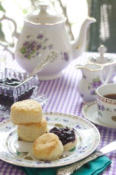 three biscuits on a plate with jam in the middle and tea pot next to it