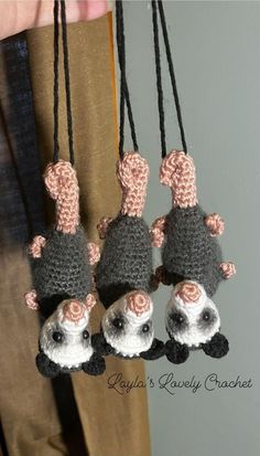 three small crocheted mice hanging from black cords with pink flowers on them, and one is wearing a hat