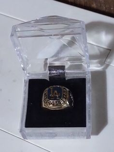 a gold ring sitting in a clear box on top of a white table with a black surface