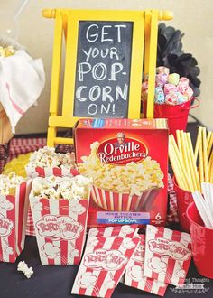 popcorn and movie tickets on a table with a chalkboard sign in the background that says get your pop corn on