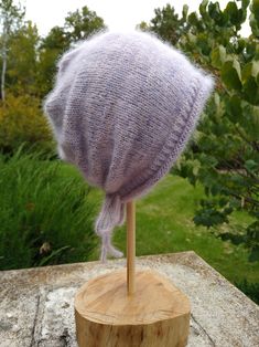 a knitted hat sitting on top of a wooden stand in front of some trees