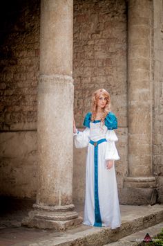 a woman dressed in medieval clothing standing next to some stone pillars with columns behind her