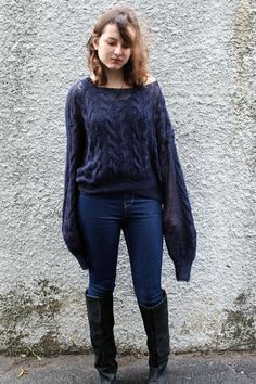 a woman standing in front of a wall wearing black boots and a sweater with an open back