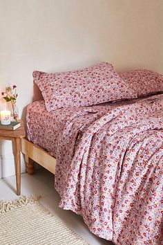 a bedroom with a bed covered in pink and white floral bedspread, two candles on end tables