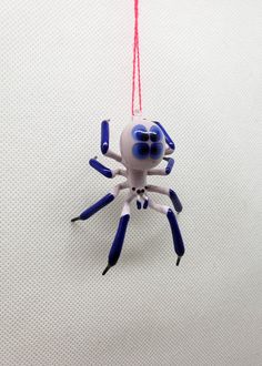 a white and blue spider toy hanging from a red string on a white surface,