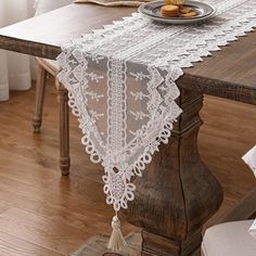 a white lace table runner sitting on top of a wooden table next to a plate