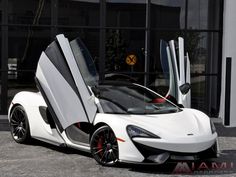 a white and black sports car parked in front of a building with its doors open