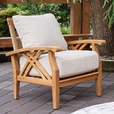 a wooden chair sitting on top of a brick floor next to a tree and bushes