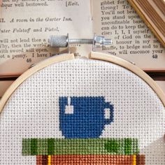 a cross stitch pattern with a coffee mug on top of a stack of books in front of an open book