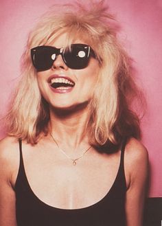 a woman with sunglasses on her face posing for a photo in front of a pink background