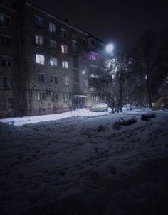 a snow covered street at night with cars parked on the side and buildings in the background