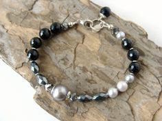 "Black and gray gemstone bracelet, agate pearls hematite and Swarovsi crystals, asymmetrical design, chunky cool bracelet Cool, elegant, a little different~ this asymmetrical handmade bracelet is a sophisticated mix of finely faceted black agate, gray-metallic hematite ovals, smooth, silvery shaded freshwater pearls, 4 darkly sparkling \"Silver Night\" Swarovski crystals and subtle sterling accents to add definition. This bracelet can shine on its own or pair with other pieces from your collecti Elegant Black Hematite Crystal Bracelet, Elegant Adjustable Hematite Crystal Bracelet, Elegant Handmade Black Pearl Bracelet, Elegant Gray Beaded Bracelets, Elegant Hematite Bracelets With Faceted Beads, Elegant Hematite Crystal Bracelet With Round Beads, Gray Gemstones, Textured Ring, Argentium Silver