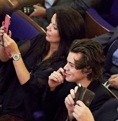 two people sitting next to each other while looking at their cell phones in the audience