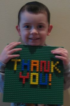 a young boy holding up a lego thank you sign