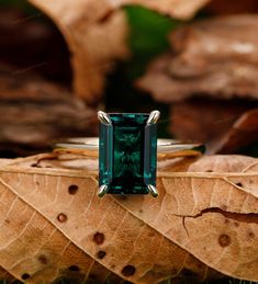 an emerald colored ring sitting on top of a leaf