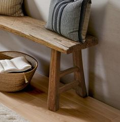 a wooden bench sitting next to a basket on top of a hard wood floor in front of a white wall