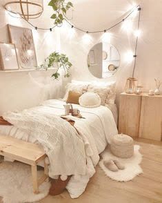 a bedroom with white walls and wooden flooring is lit by fairy lights, while a bed sits in front of a mirror on the wall