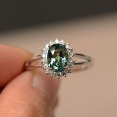 a close up of a person's hand holding a ring with a green stone