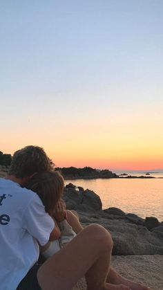 two people are sitting on the beach at sunset