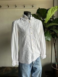 Vintage White Cotton Eyelet Long Sleeve Blouse. White in color made from all cotton fibers. Eyelet accents throughout blouse. Front button up closure with high neck fit. Very soft and lightweight with a relaxed fit. Condition overall is good with only minor flaws that include; blouse has very light underarm spotting as shown in photos. No rips or tears. Please see all photos for details.  Refer to measurements below to ensure a proper fit (modeled on a size medium mannequin) fits true to size 19" pit to pit 15" shoulder to shoulder 24" sleeves 26" in length Long Sleeve Off-white Cotton Blouse, Vintage Long Sleeve Blouse In Vintage White, White Button-up Eyelet Blouse, Victorian White Long Sleeve Blouse, Elegant Button-up Blouse With Broderie Anglaise, White Cotton, Cotton Fiber, White Vintage, Womens Clothing Tops