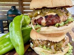 three hamburgers stacked on top of each other with peppers next to them and a bbq grill in the background