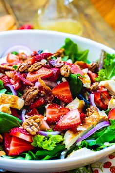 a salad with strawberries, onions and walnuts in a white bowl on a table