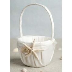 a white basket sitting on top of a sandy beach next to shells and starfish