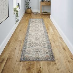 a long hallway with wooden floors and white walls has a large rug on the floor