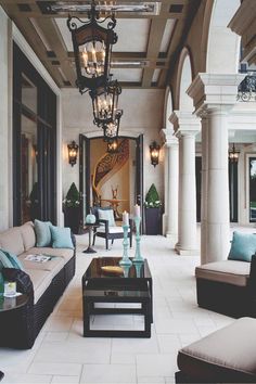 a living room filled with lots of furniture next to a tall ceiling light hanging from a chandelier