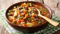 a bowl of soup with meat, potatoes and carrots on a green checkered napkin