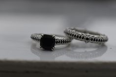 two rings sitting on top of a white table next to each other with black stones