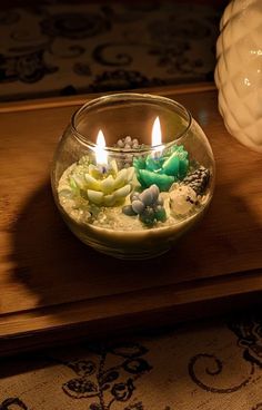 two lit candles sitting in a bowl filled with rocks and pebbles on a wooden table