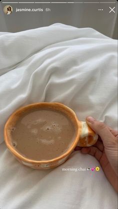 someone is holding a cup of hot chocolate in their hand while laying on the bed