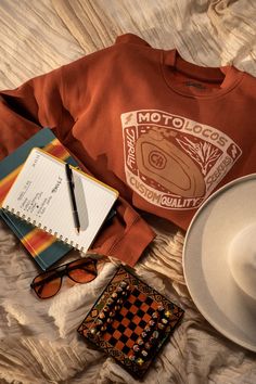 a hat, sunglasses, notebook and other items are laid out on a white blanket