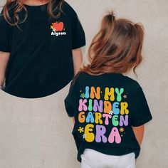 In My Kindergarten Era Shirt, Custom Kindergarten Shirt, First Day Of School, Back To School Shirt, Hello School Shirt, 1st Grade Tee Note: For Different Color From Colors List Please "Message us or leave a note" MATERIAL UNISEX T-SHIRT - Medium fabric (5.3 oz/yd² (180 g/m - Classic fit - Runs true to size - 100% cotton (fiber content may vary for different colors) - Tear-away label UNISEX SIZING CHART Small: Length 28" - Width 18" (4-6) Medium: Length 29" - Width 20" (6-10) Large: Length 30" - Width 22" (10-14) XL: Length 31" - Width 24" (14-18) 2XL: Length 32" - Width 26" (18-20) 3XL: Length 33" - Width 28" (20-22) All measurements are approximations. Shirts may be within 1" of the dimensions listed The shirts were measured laying on a flat surface, side to side and top to bottom. HOW TO Kindergarten Shirts For Kids First Day, First Day Of School Shirts Kids, First Day Of Pre K Shirt, Cute School Tops With Name Print, Cute T-shirt With Name Print For Teacher Appreciation, Short Sleeve Tops With Name Print For Daycare, Cute Letter Print Shirt For Daycare, Cute Tops With Name Print For Teacher Appreciation, Customizable Cute Tops For School